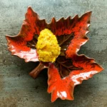 En portion gul hjemmelavet pickles anrettet i en rød og brun keramikskål formet som et efterårsblad.