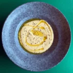 Hummus med olivenolie i blå skål på grøn baggrund