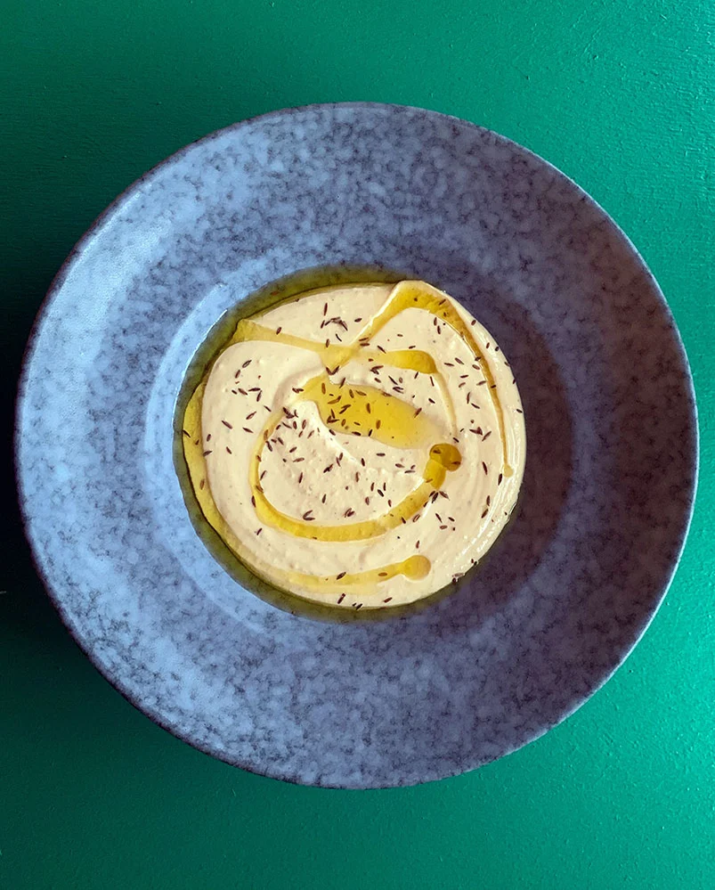 Hummus med olivenolie i blå skål på grøn baggrund
